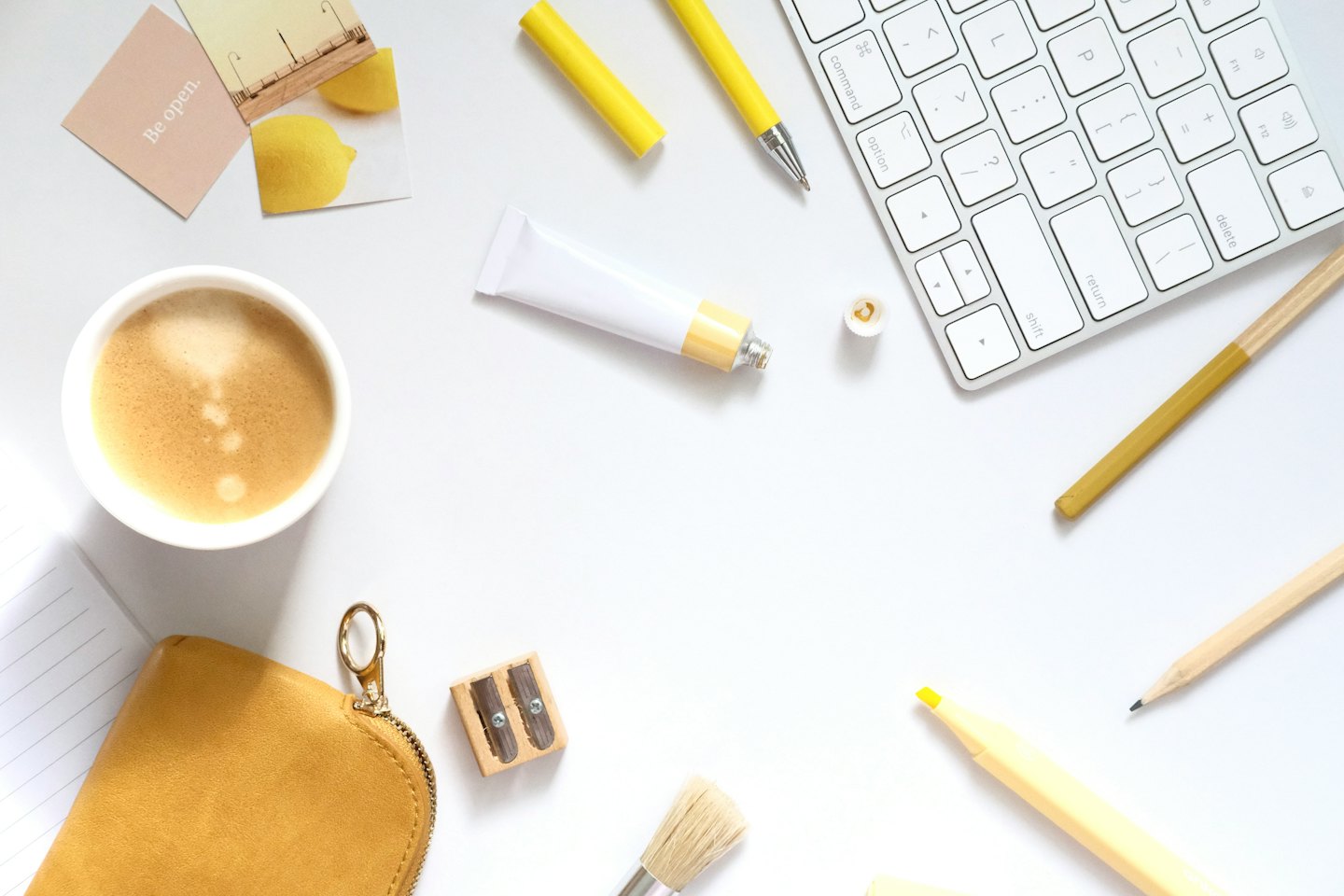 Vista dall'alto di caffè, tastiera, penne e materiale artistico su una scrivania.