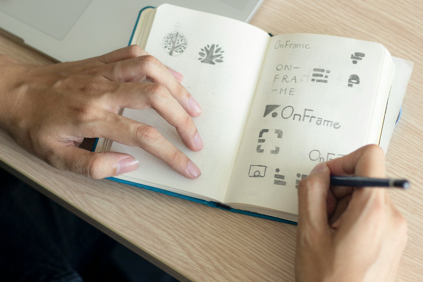 Mani che disegnano bozzetti di loghi su un taccuino su una scrivania.
